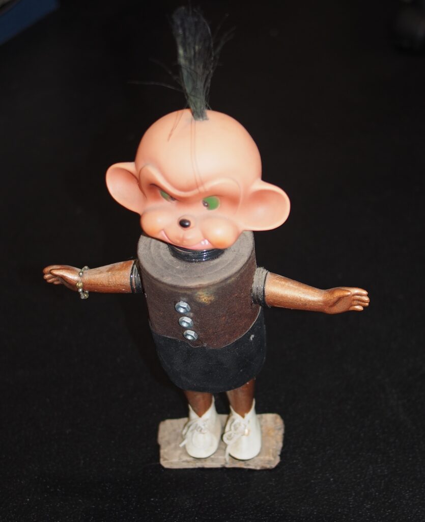 The Angry Monkey standa with his soup can body, and his dolls head, a pony tail sprouts from the top of his head.